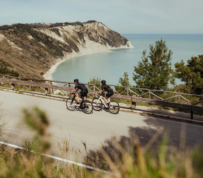 Un villaggio nelle Marche sul mare: il Natural Village Resort Due ciclisti in abbigliamento sportivo su strada con scogliera e mare sullo sfondo