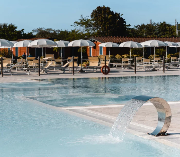 Un villaggio nelle Marche sul mare: il Natural Village Resort Piscina con ombrelloni bianchi e sedie a sdraio in un'area relax all'aperto