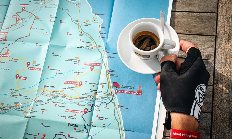 What could be better than a bike hotel in the Marche region? Hand with glove holding coffee cup over detailed map of Italian towns