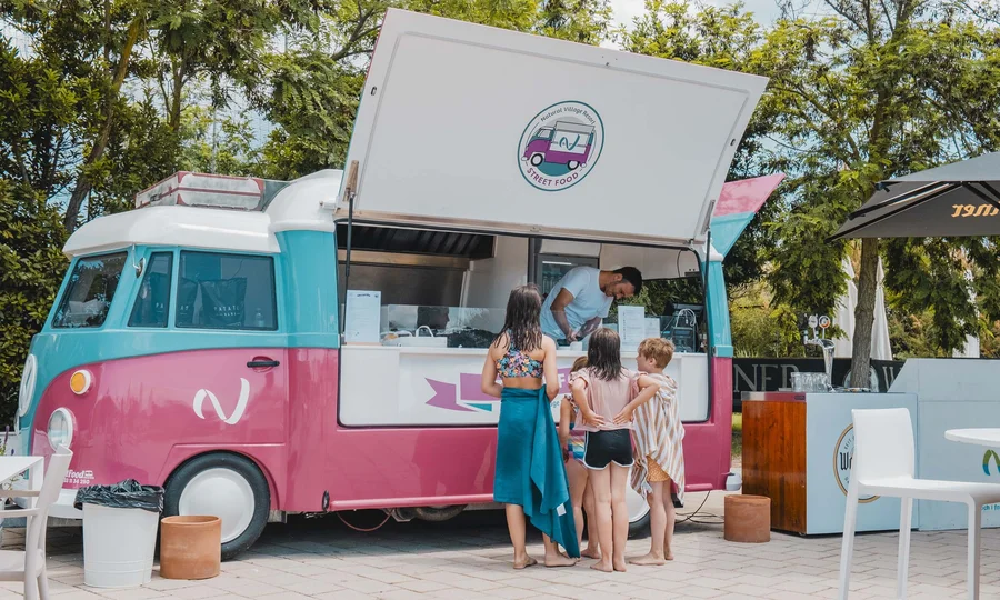 Un villaggio nelle Marche sul mare: il Natural Village Resort Bimbi in costume ordinano al food truck rosa e azzurro all'aperto vicino a tavoli