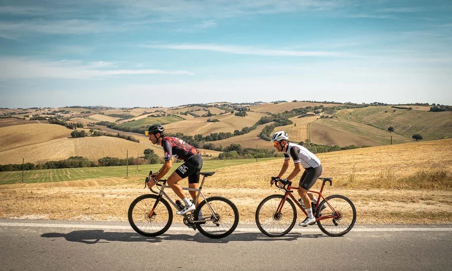 What could be better than a bike hotel in the Marche region? Two cyclists riding on flat road with dry hilly landscape in background