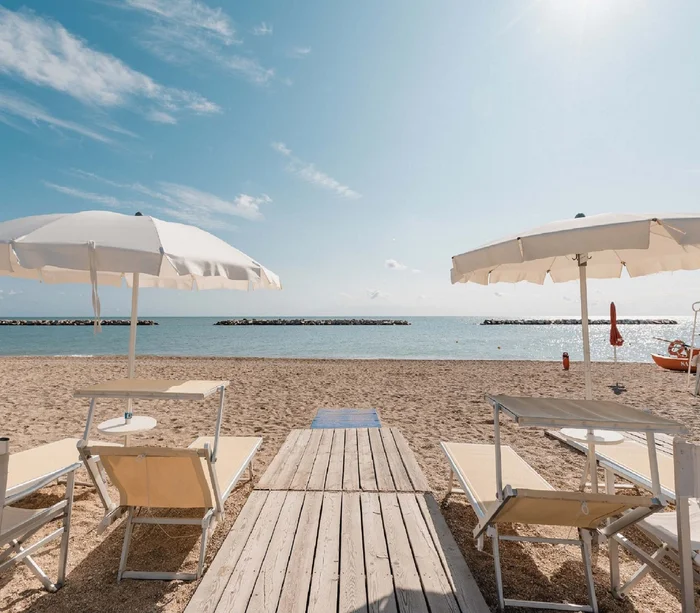 Un villaggio nelle Marche sul mare: il Natural Village Resort Lettini e ombrelloni beige su spiaggia sabbiosa con vista sul mare calmo
