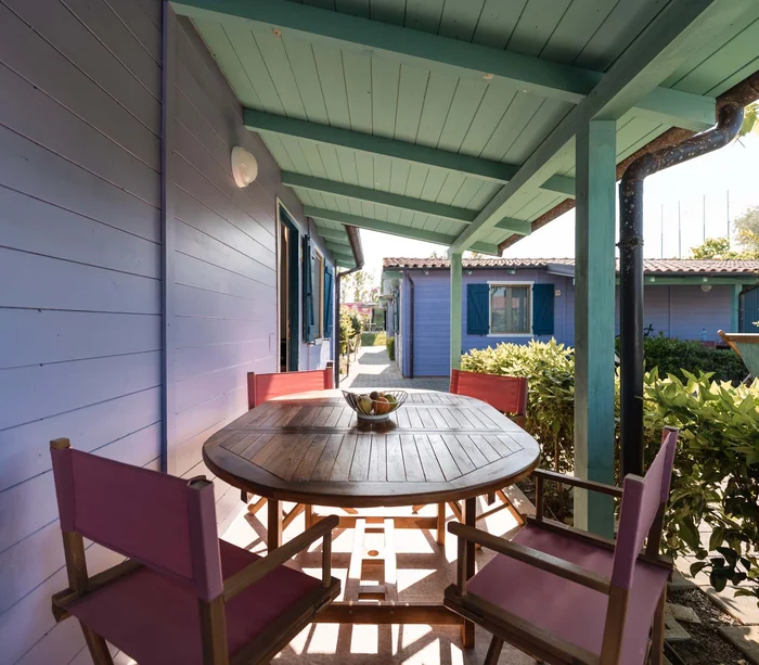 Un villaggio nelle Marche sul mare: il Natural Village Resort Terrazza coperta con tavolo in legno e quattro sedie rosse davanti a case di legno blu