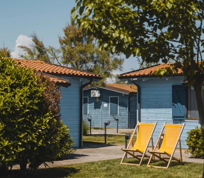 Un villaggio nelle Marche sul mare: il Natural Village Resort Due sedie sdraio arancioni vicino a casette di legno blu sotto alberi verdi
